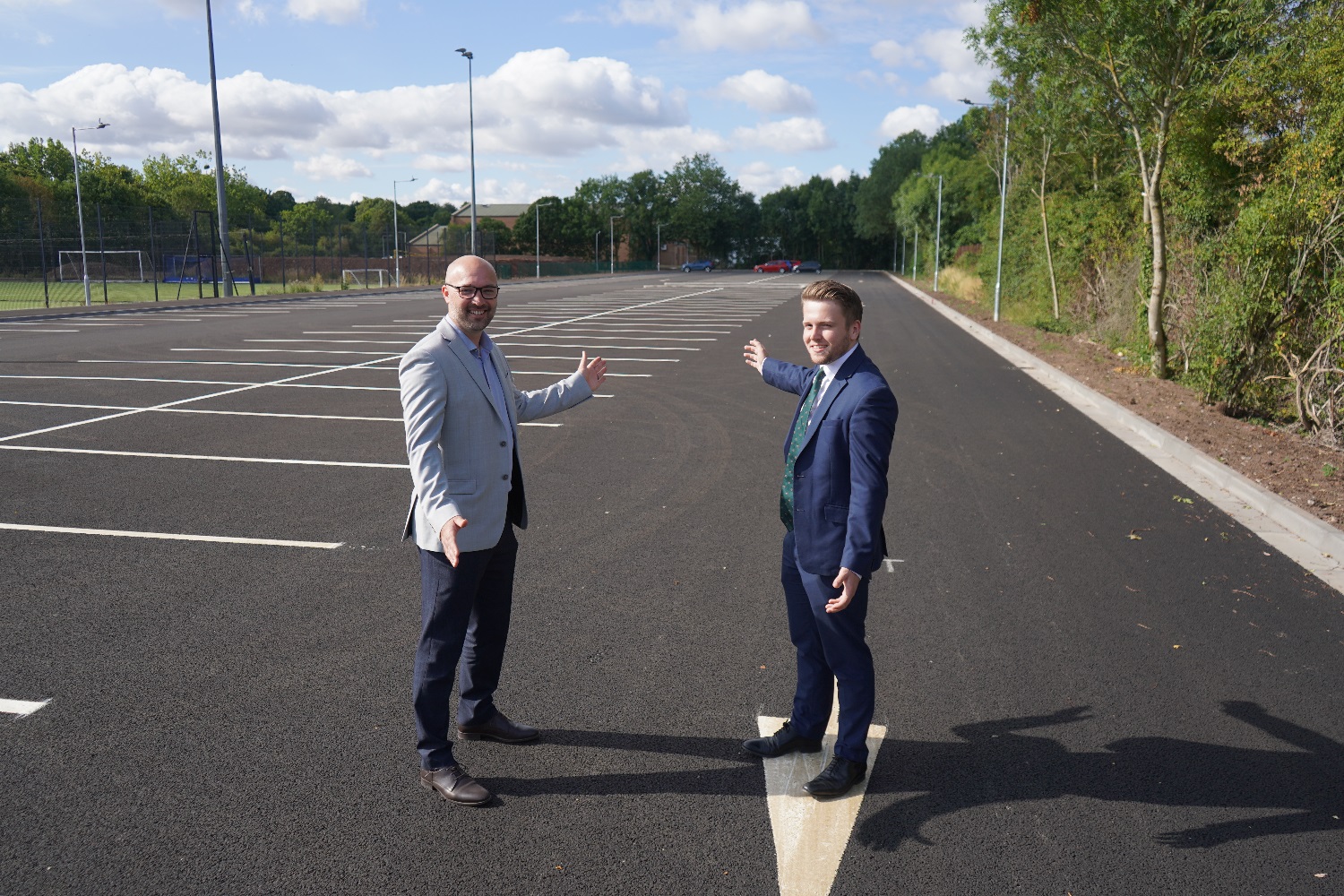 Two men stood in a car park with trees and a leisure centre in the background.