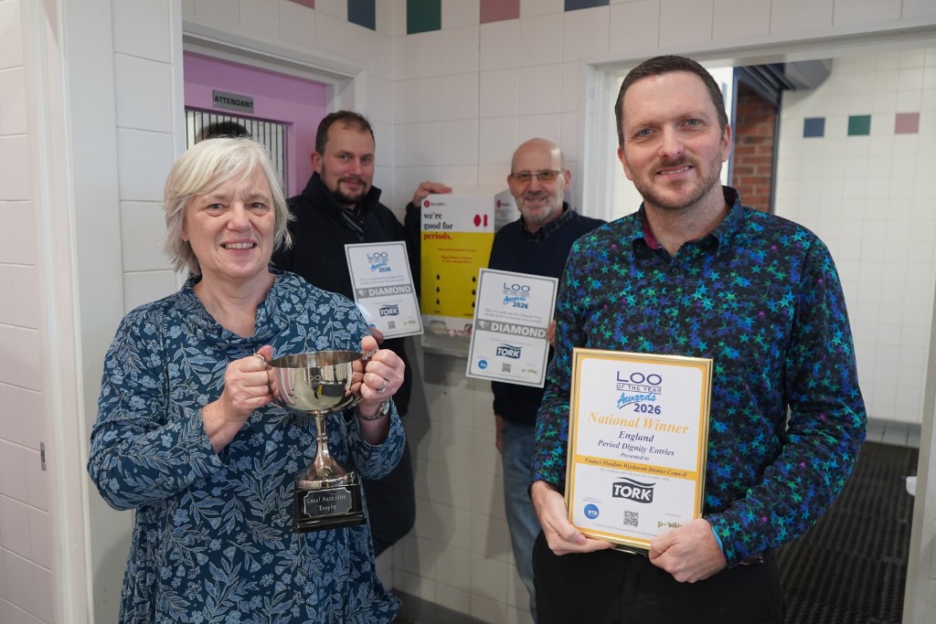 A group of people holding a trophy and certificates in a public toilet