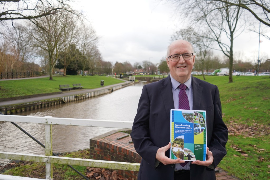 Cllr Morris stood on a bridge over a canal in Droitwich Spa holding the Transforming Worcestershire document