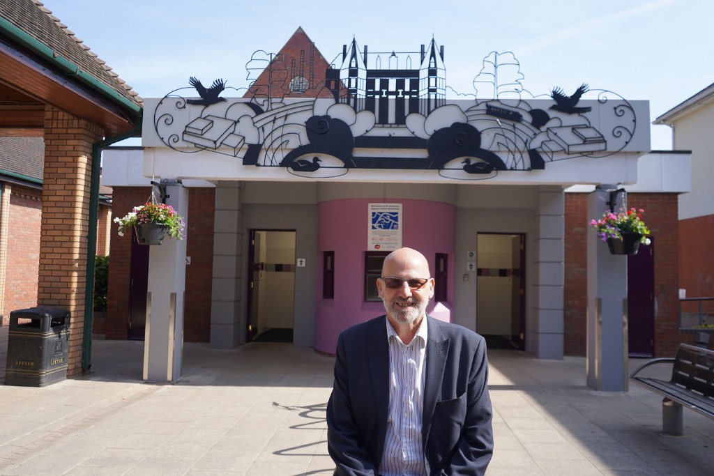 A man sat outside the front of some public toilets