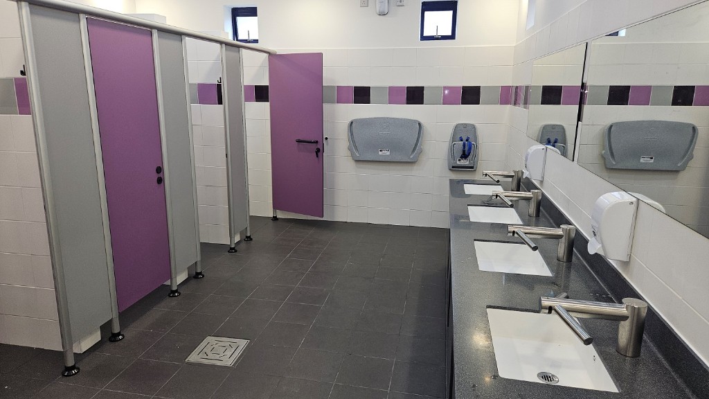 An inside shot of some cubicles and wash basins with mirrors above them.
