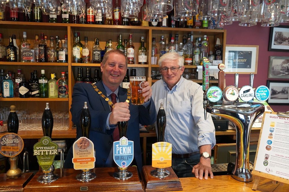 Cllr Raphael stood behind a bar holding a pint with another man next to him