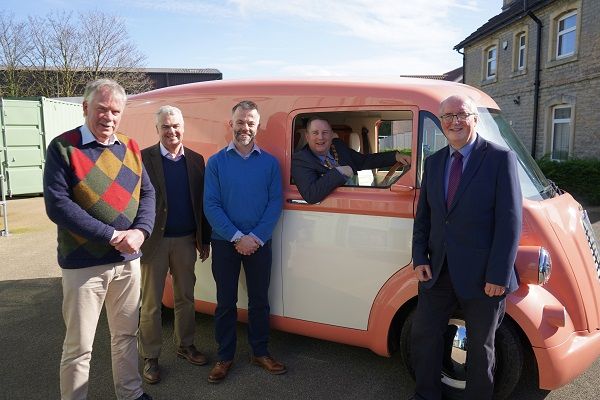 Four men stood either side of a pink van with a man inside leaning out the window.