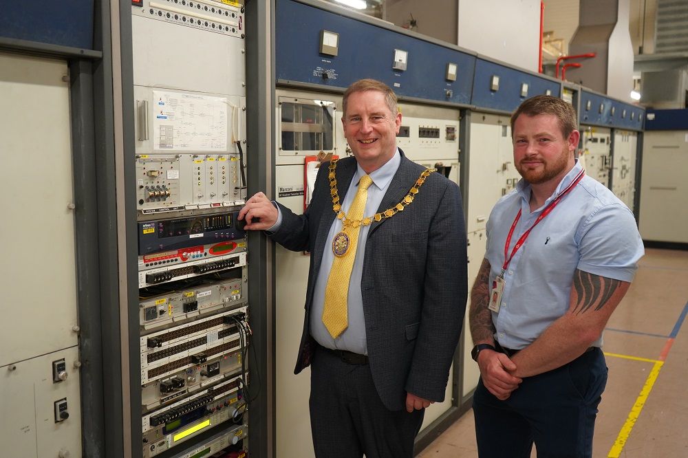 Cllr Robert Raphael turning a switch on a transmitter with Nathan McComish standing behind him.