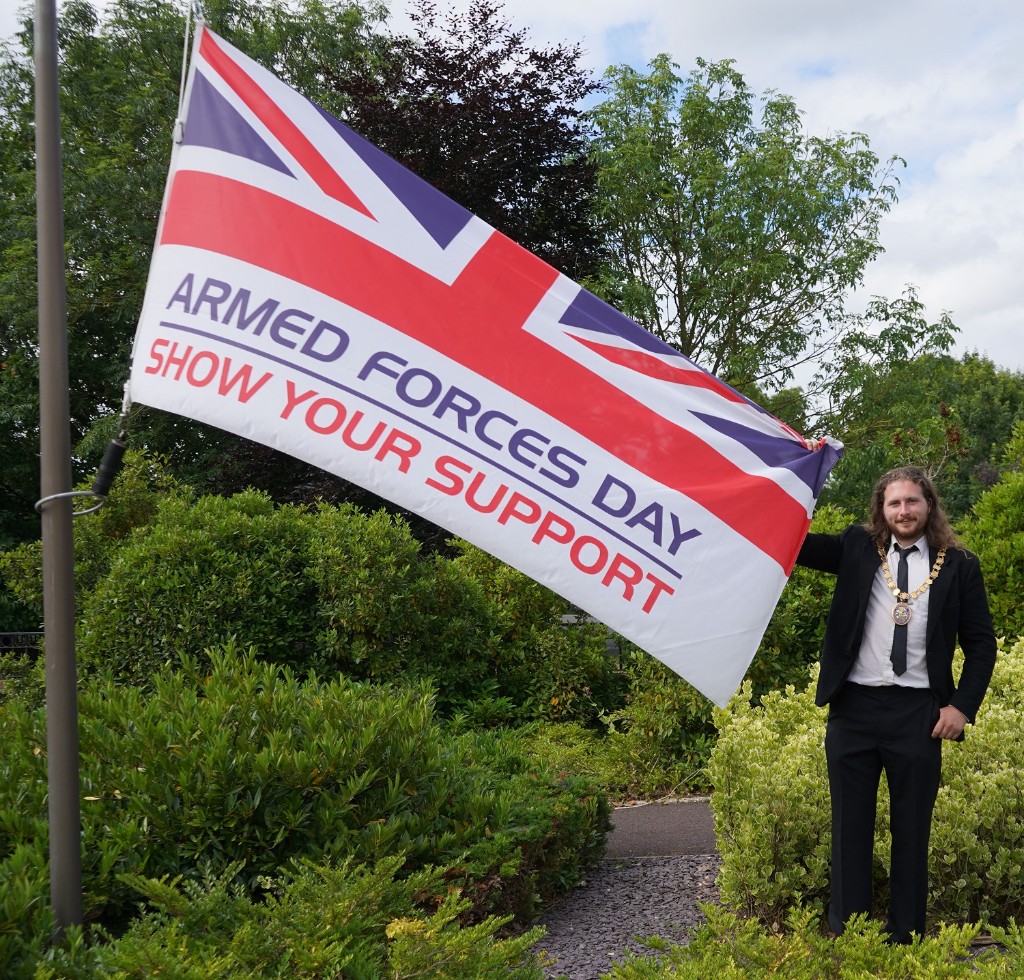 Cllr George Duffy holding the Armed Forces Day flag which has the Union Flag at the top and then the slogan Armed Forces Day Show Your Support
