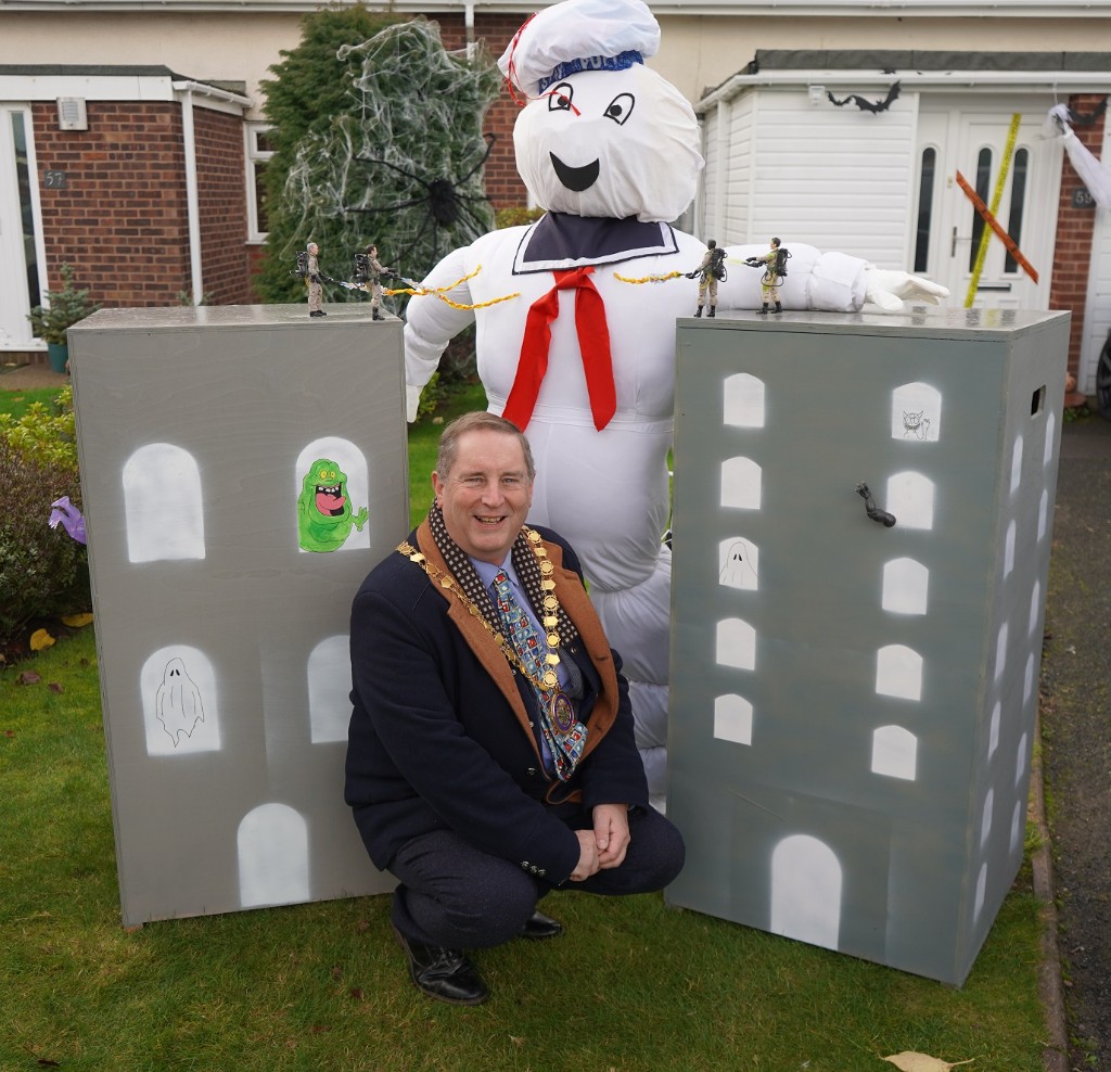 A man knelt down between two carboard replicas of tower blocks and the Staypuft man from the film Ghostbusters in the background.