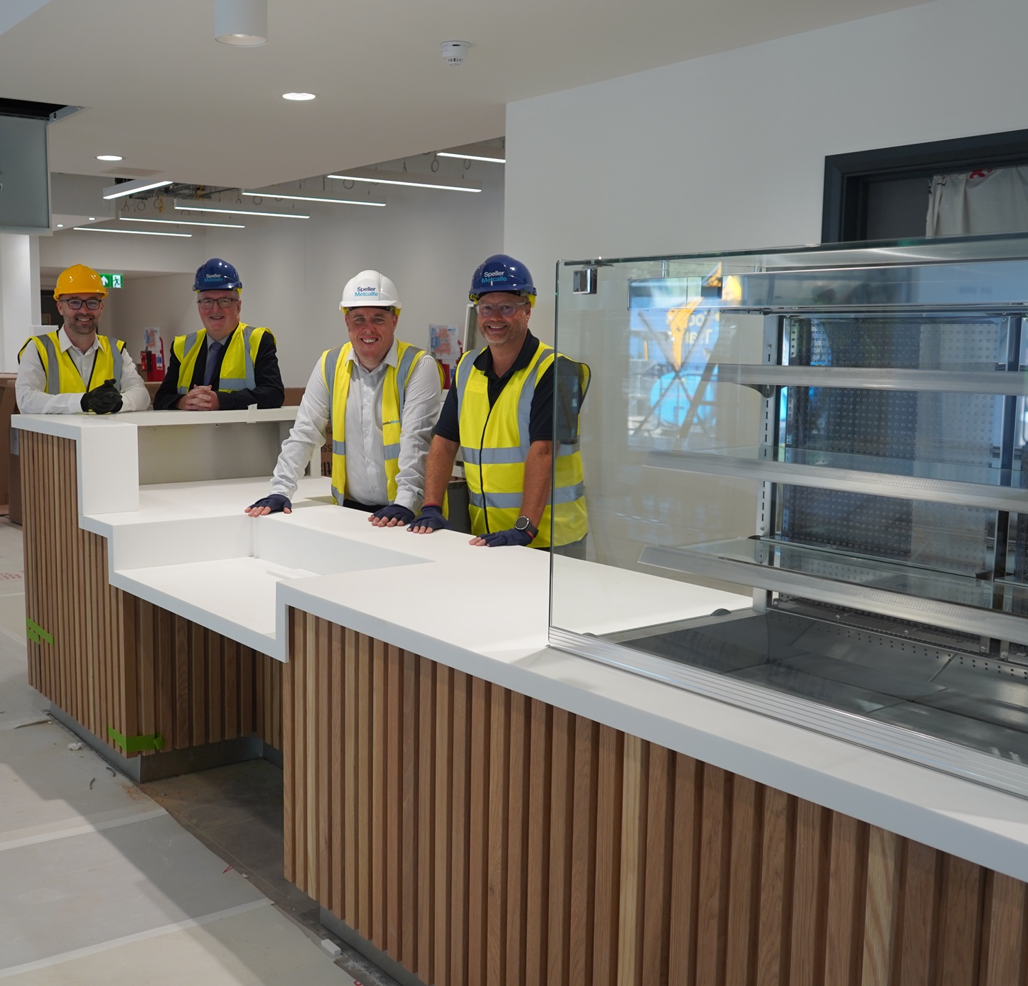 A group of people in hard hats and hih vis in front of a servery area