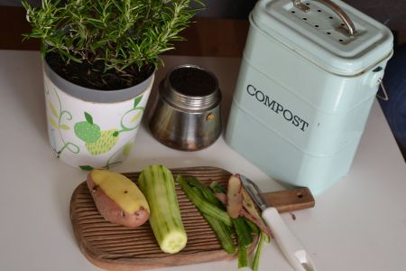 Peeled potato and cucumber on a wooden chopping board next to waste peelings